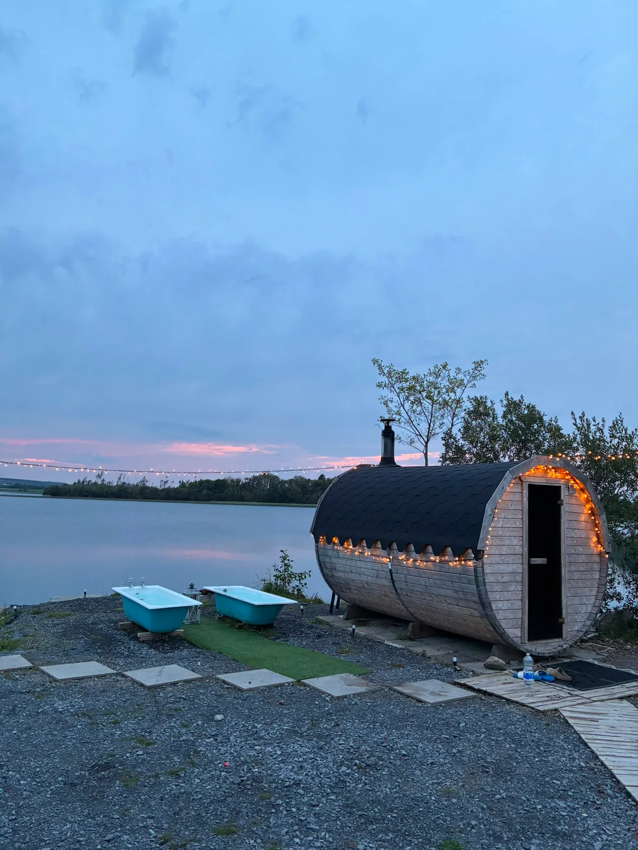 The barrel sauna lit by fairy lights beneath a soft blue evening sky