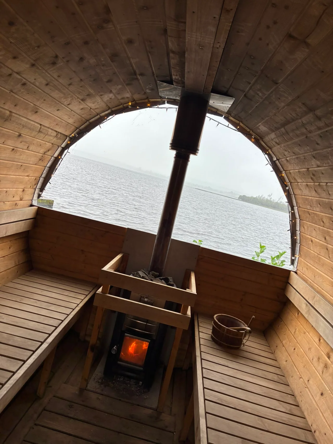 Timber benches, a wood bucket and a lit stove inside the sauna