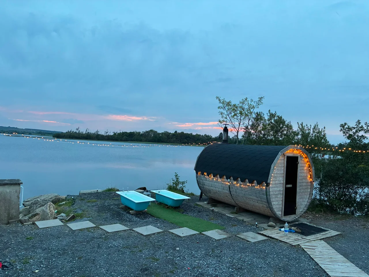 The sauna with its fairy lights on beside calm evening water