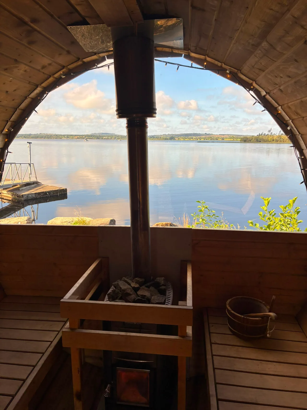 Still water and clouds seen through the curved sauna window