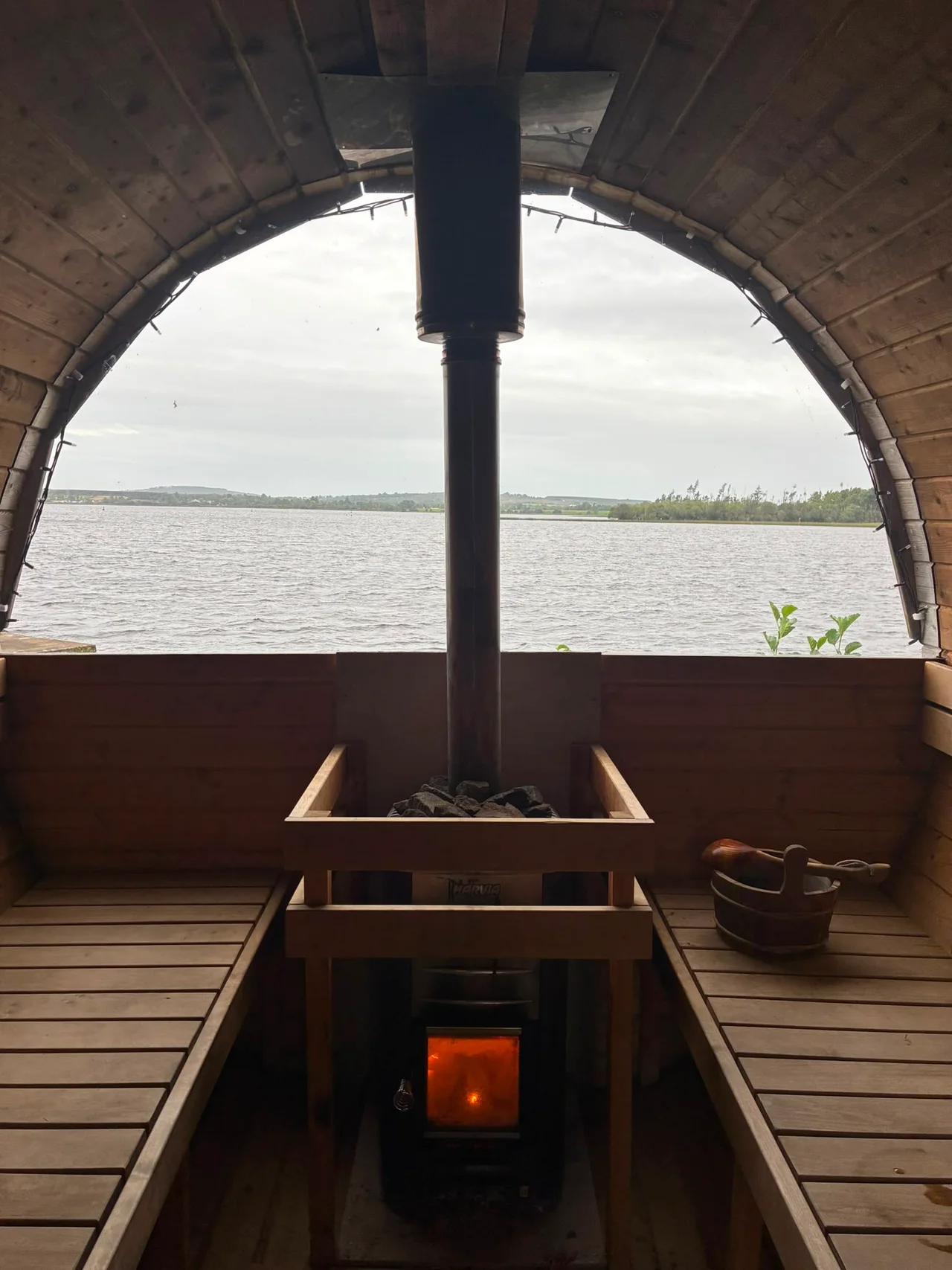 The stove, bucket and curved window inside the sauna on a cloudy day